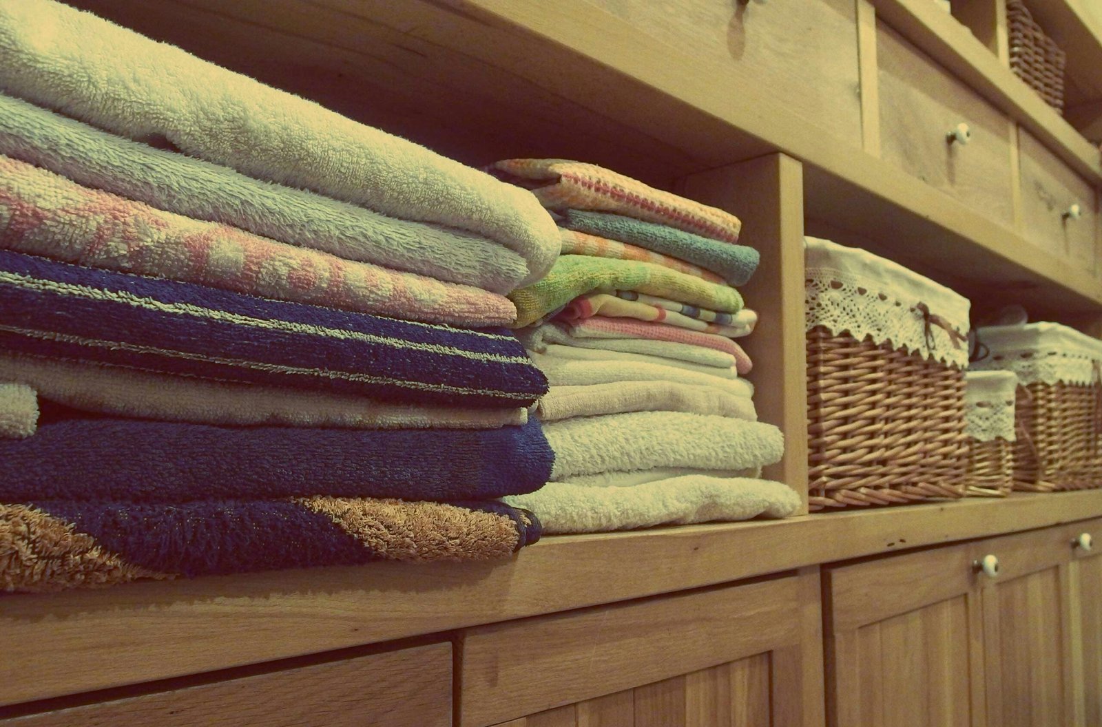 Home Tidy wooden cabinet with neatly stacked towels and decorative baskets in an indoor setting.